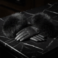 Black leather glove with fur cuff on a textured surface