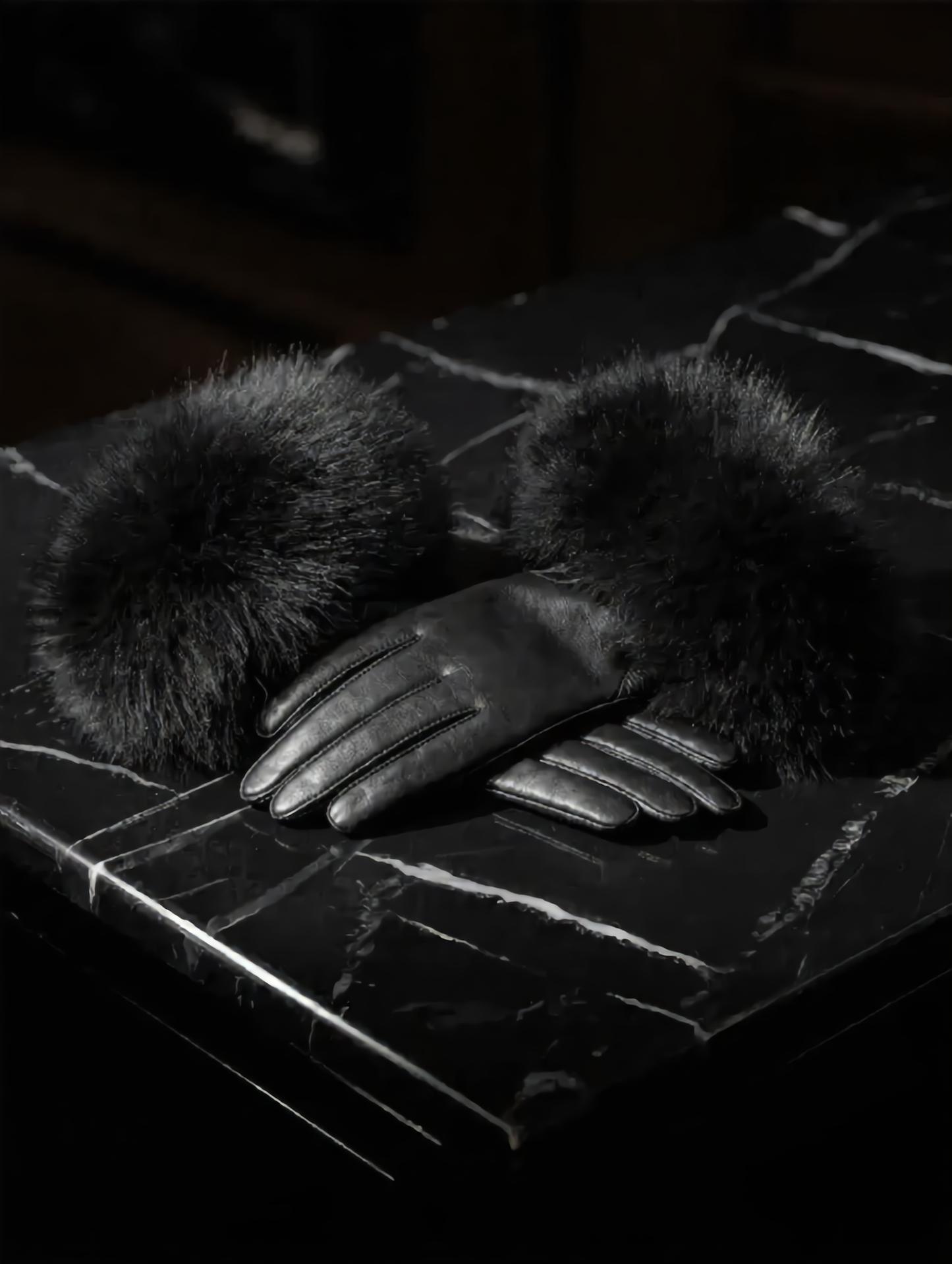 Black leather glove with fur cuff on a textured surface