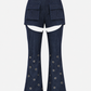 A pair of dark blue denim flared pants with front flap pockets at the waist and circular metal grommet details down the legs, shown against a plain light gray background.