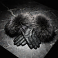 Pair of black leather gloves with fur pom-poms on a dark stone surface