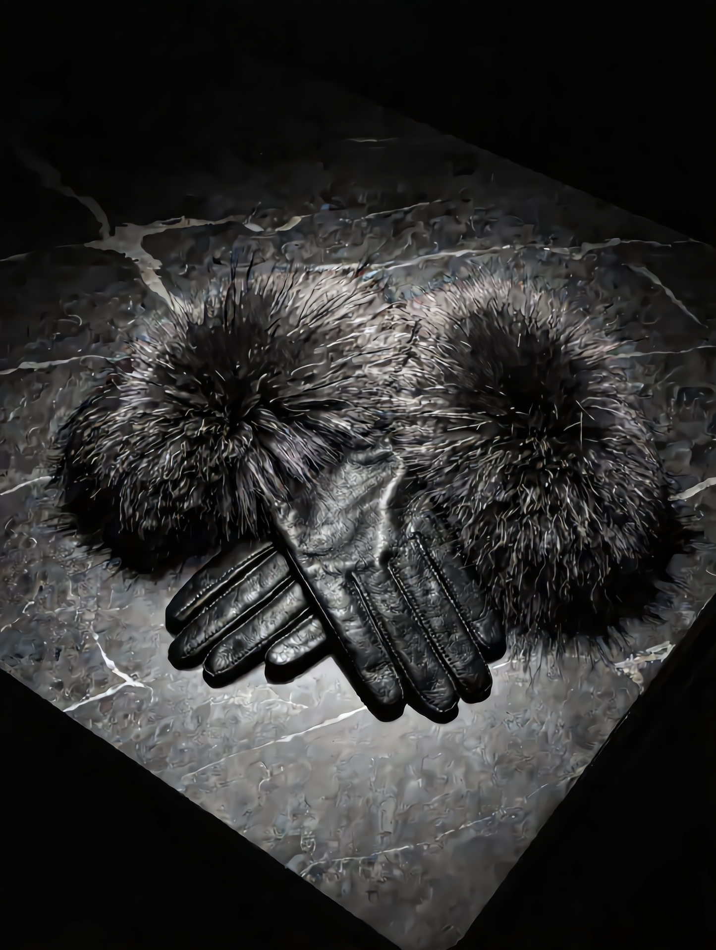 Pair of black leather gloves with fur pom-poms on a dark stone surface