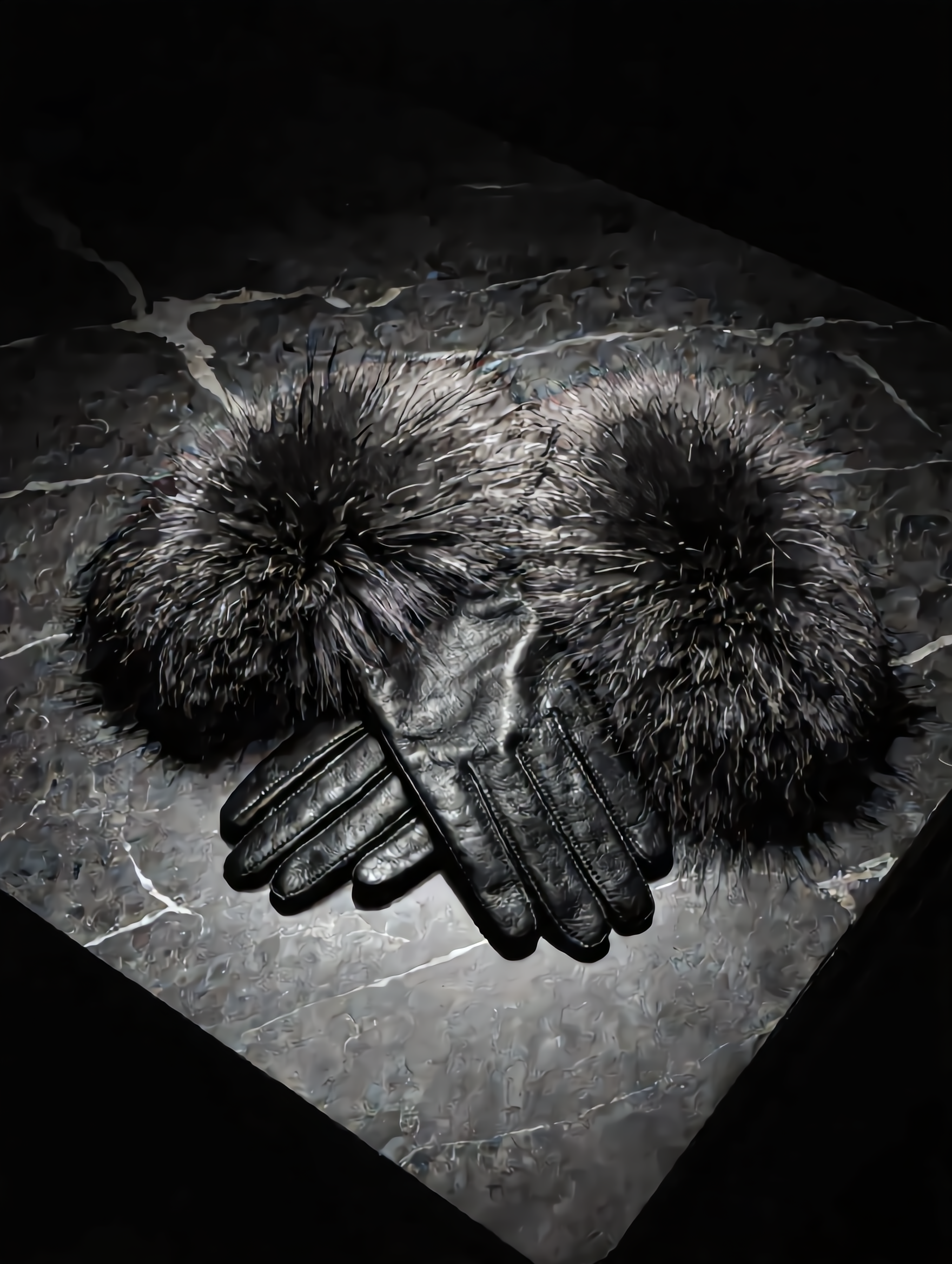 Pair of black leather gloves with fur pom-poms on a dark stone surface