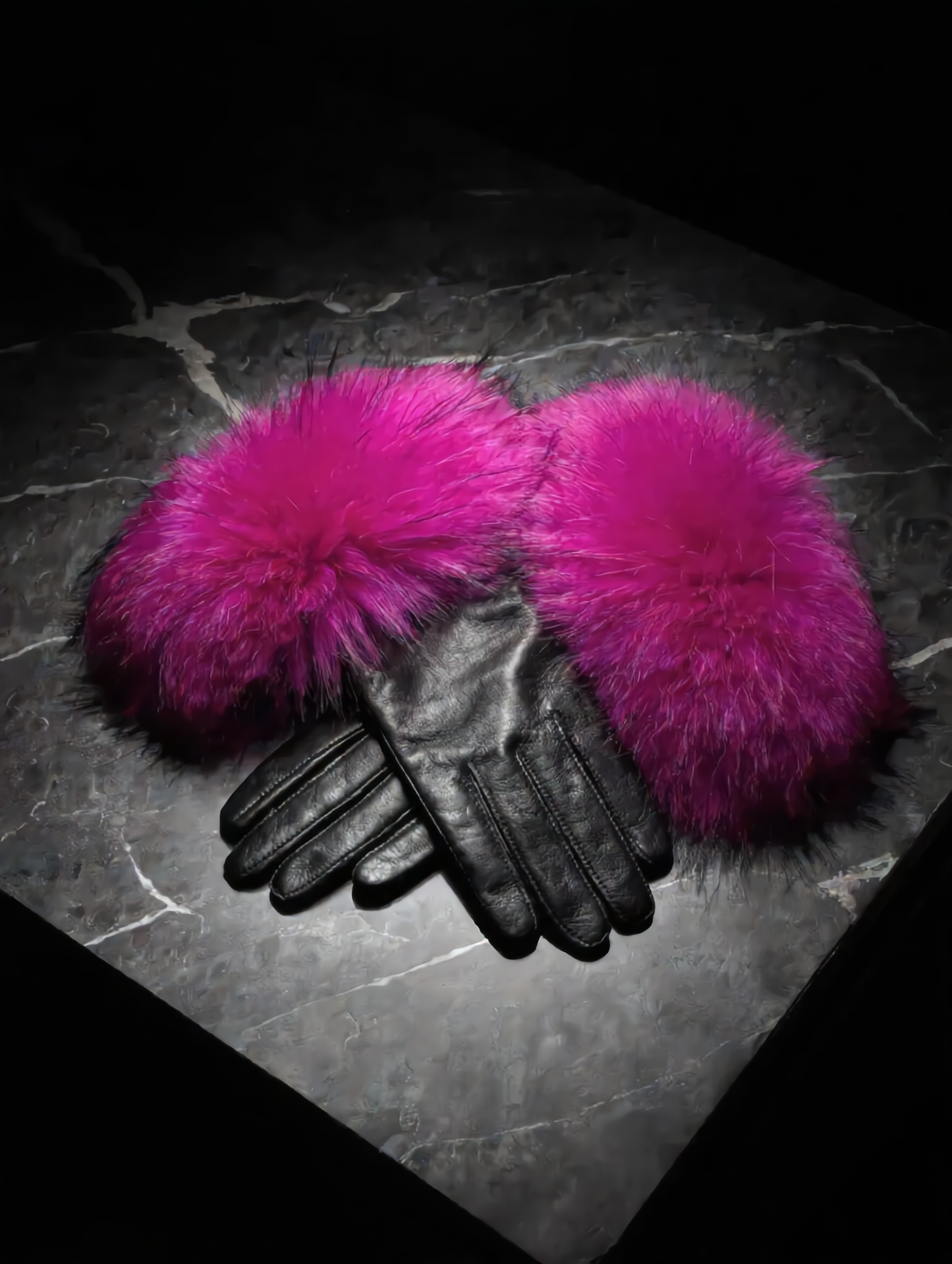 Black gloves with bright pink fur cuffs on a dark textured surface